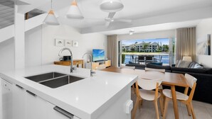 Une cuisine moderne dotée d’un grand îlot central, un coin repas avec une table et des chaises, et un salon avec un canapé et un téléviseur.