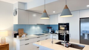 Une cuisine moderne avec des armoires blanches, un four encastré, un réfrigérateur en acier inoxydable et des luminaires suspendus.