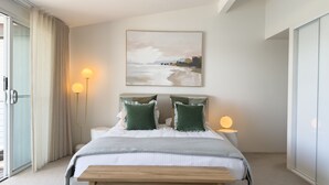 Une chambre à coucher avec un lit, des lampes de chevet, un tableau et une vue sur l’extérieur, visible à travers une porte coulissante.
