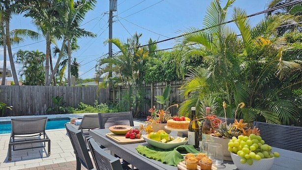 Un área de comedor al aire libre con piscina, rodeada de palmeras y una valla de madera.