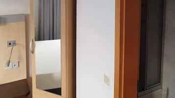 Une pièce comprenant une armoire en bois, un miroir, un petit bureau avec une lampe et une fenêtre avec un rideau.