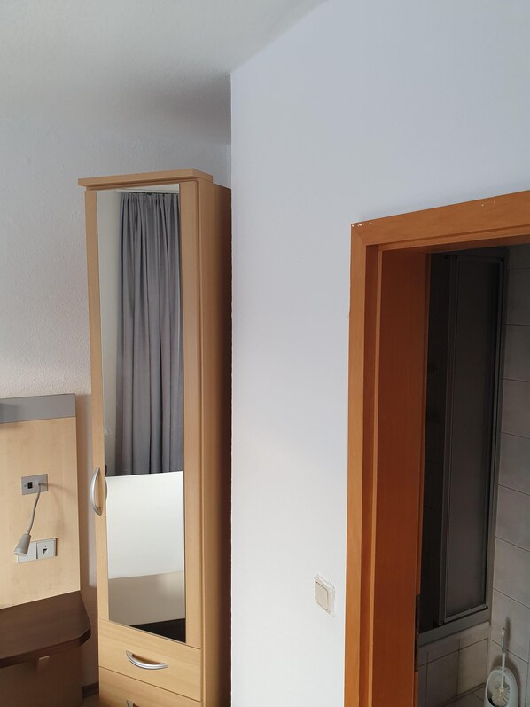 A room with a wooden wardrobe, a mirror, a small desk with a lamp, and a window with a curtain. - Stettiner Hof (Eggesin)