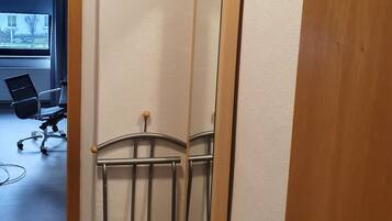 A room with a large mirror, a metal bed frame, and a wooden door.