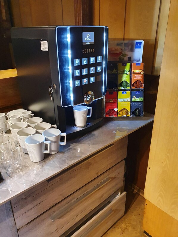 A coffee machine with a digital interface, multiple coffee cups, and boxes of coffee pods on a wooden counter. - Stettiner Hof (Eggesin)