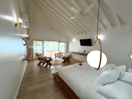 Amplia habitación con una cama grande, ventilador de techo, televisión y vista a la playa.