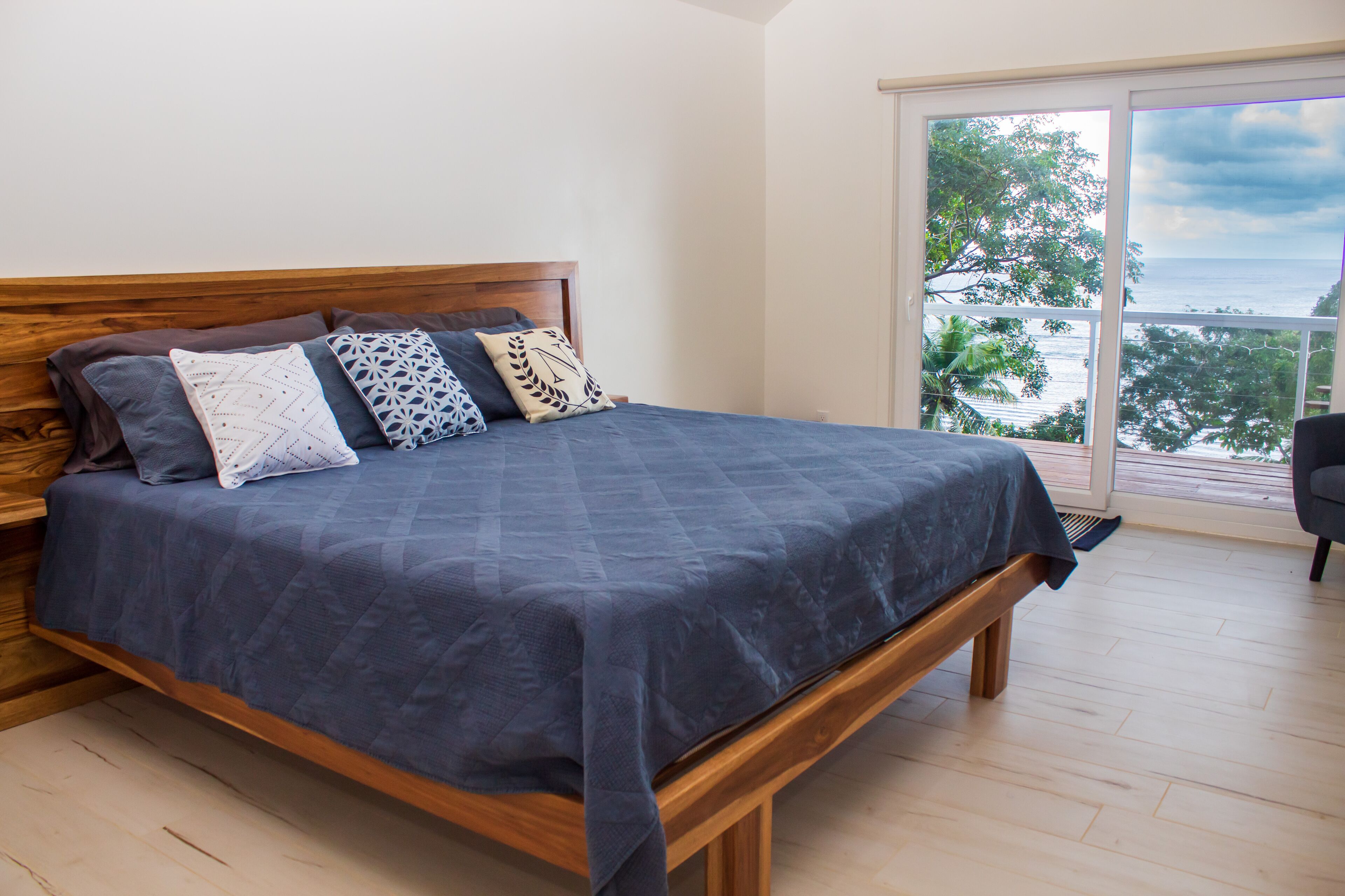 Un dormitorio con cama de madera, vista al océano y balcón.