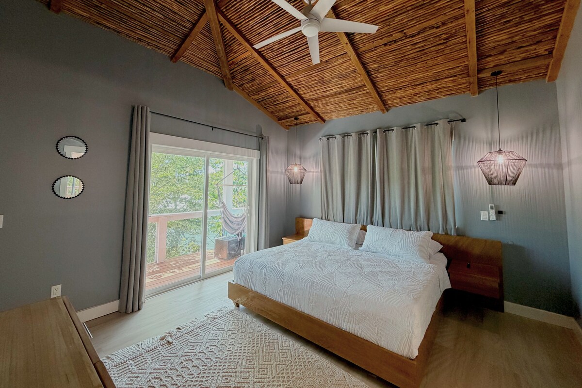 Un dormitorio con una cama grande, un ventilador de techo y vistas al exterior a través de un ventanal corredero.