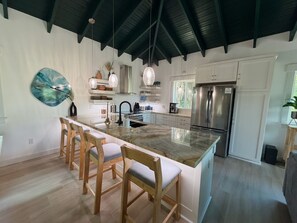 A modern kitchen with a central island, wooden chairs, a stainless steel refrigerator, and pendant lighting. - Luna Beach (Roatan)