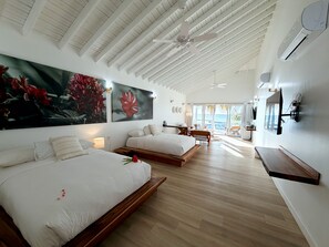 A hotel room with two beds, a ceiling fan, a large window with a view, and a mounted TV. - Luna Beach (Roatan)