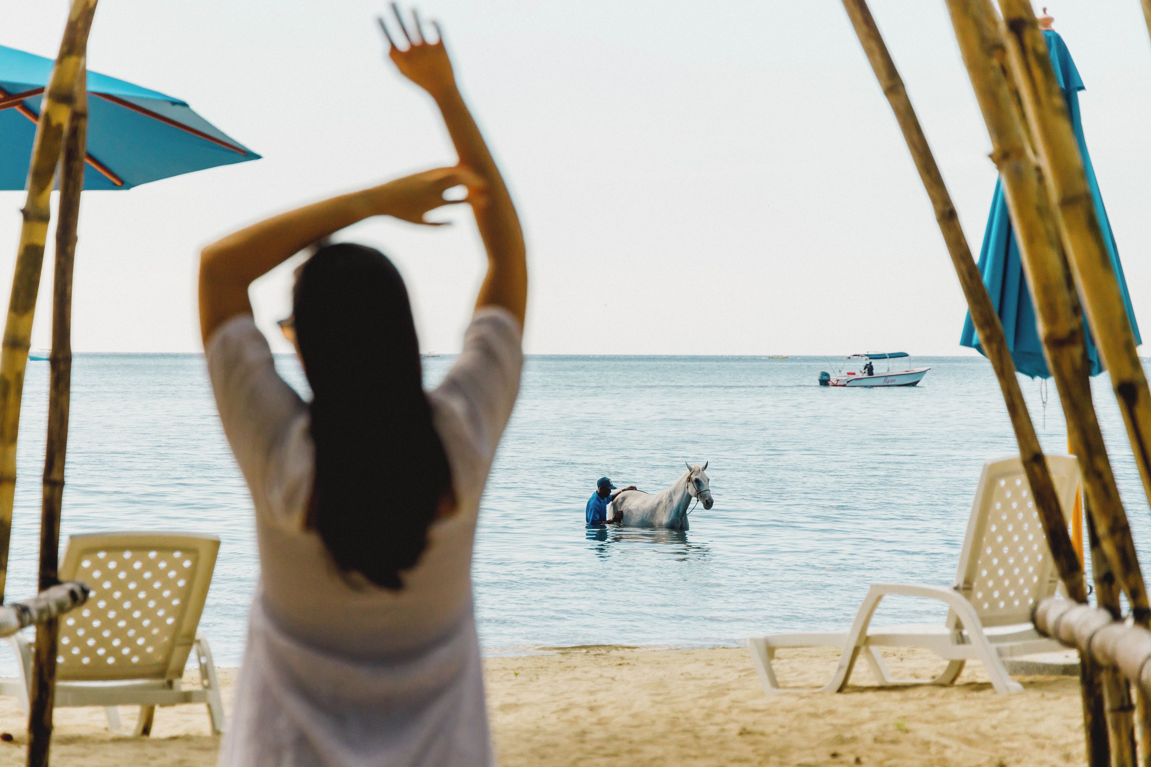 A beach scene with a person in the water, a boat, and beach chairs.