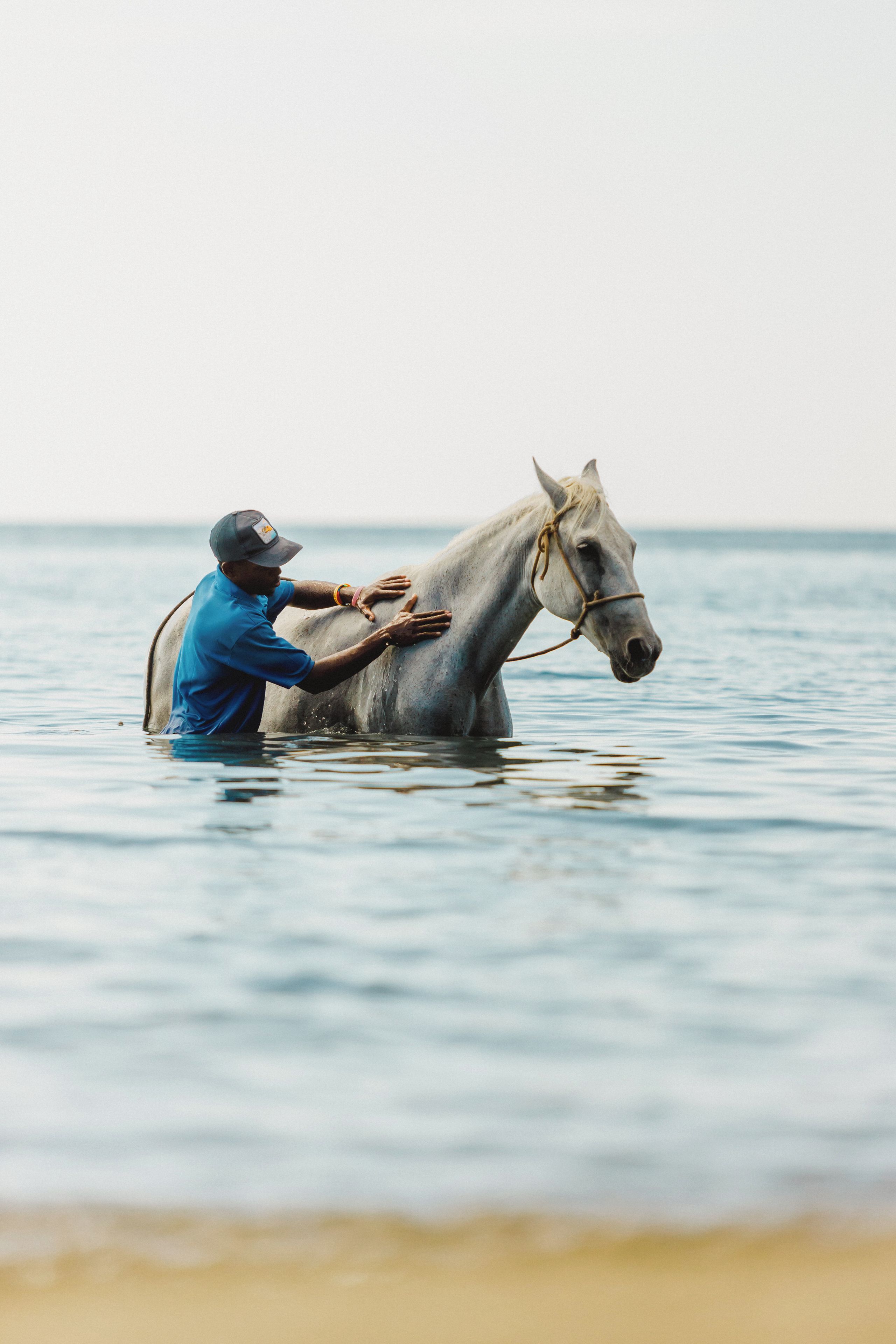 A person in blue attire leading a horse through water.