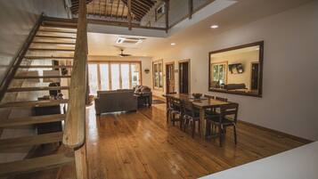 Una habitación amplia con una escalera de madera, un comedor con mesa y sillas, y un espejo grande en la pared.