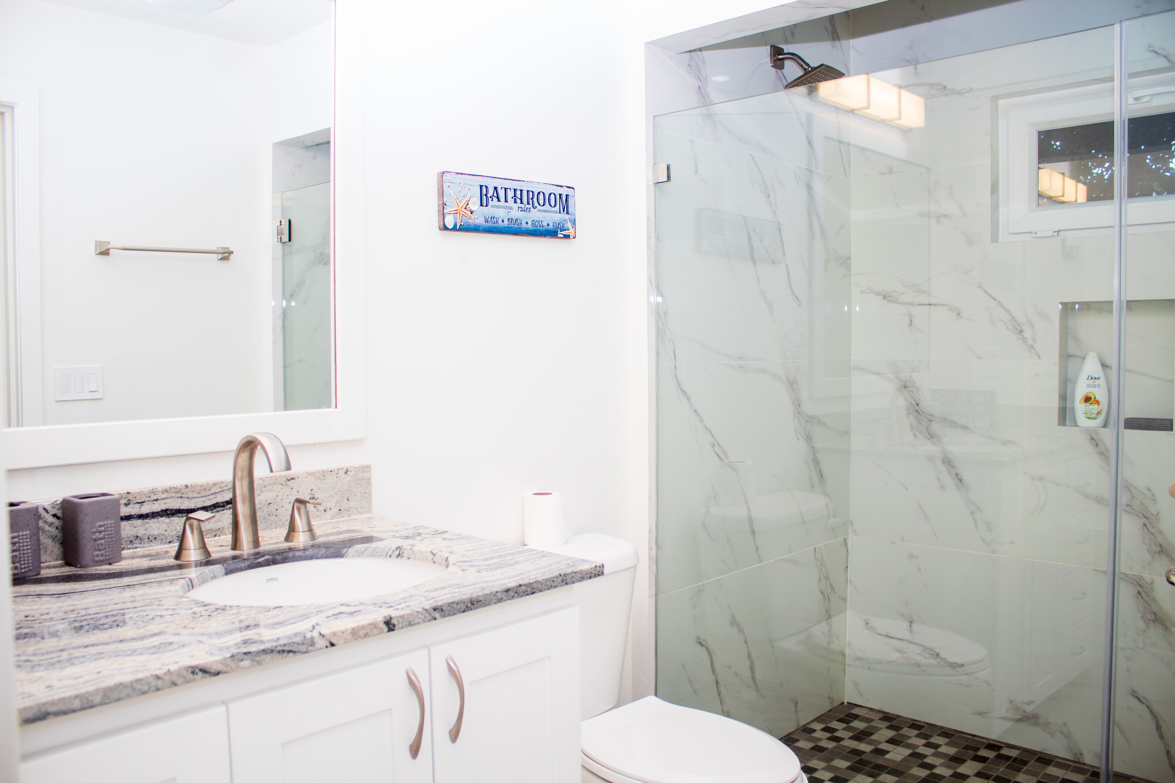 Un baño con lavamanos de mármol, cabina de ducha con mampara de vidrio y un inodoro.