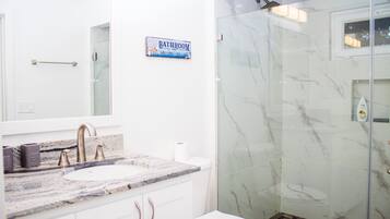 Un baño con lavamanos de mármol, cabina de ducha con mampara de vidrio y un inodoro.
