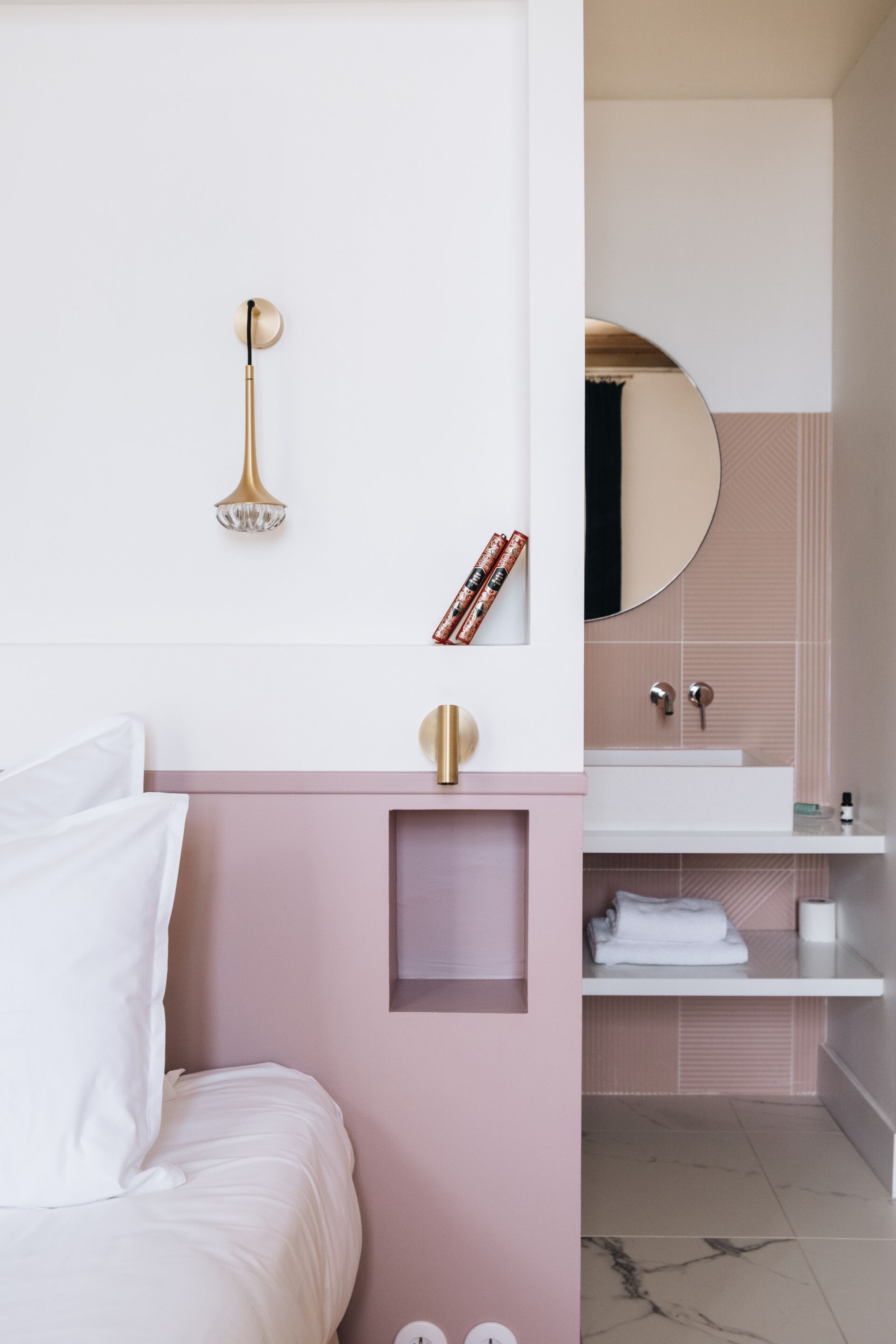 Un dormitori modern amb un llit, una taula de nit, una làmpada penjada a la paret i un bany amb un lavabo i un mirall.