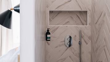 A modern shower with a herringbone tile pattern, a handheld showerhead, and a bottle of shampoo.