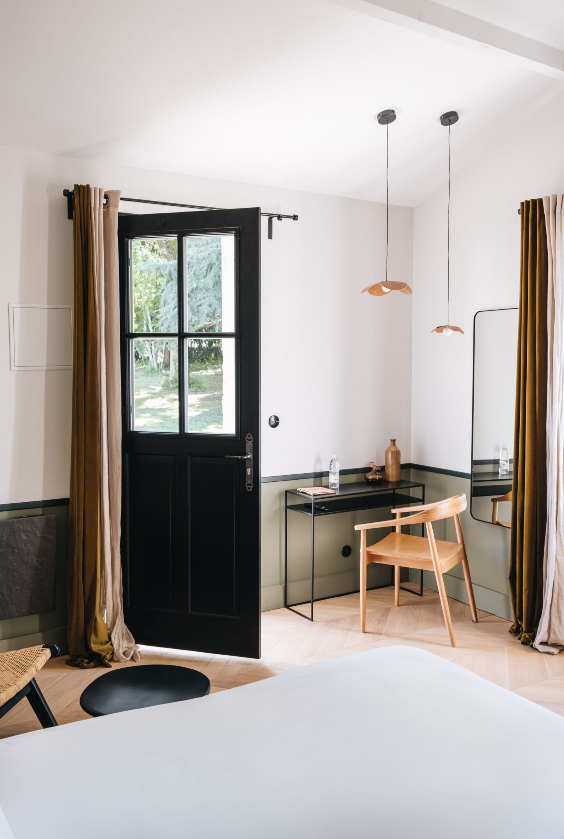 A room with a black door, a desk, a chair, a bed, and a mirror.