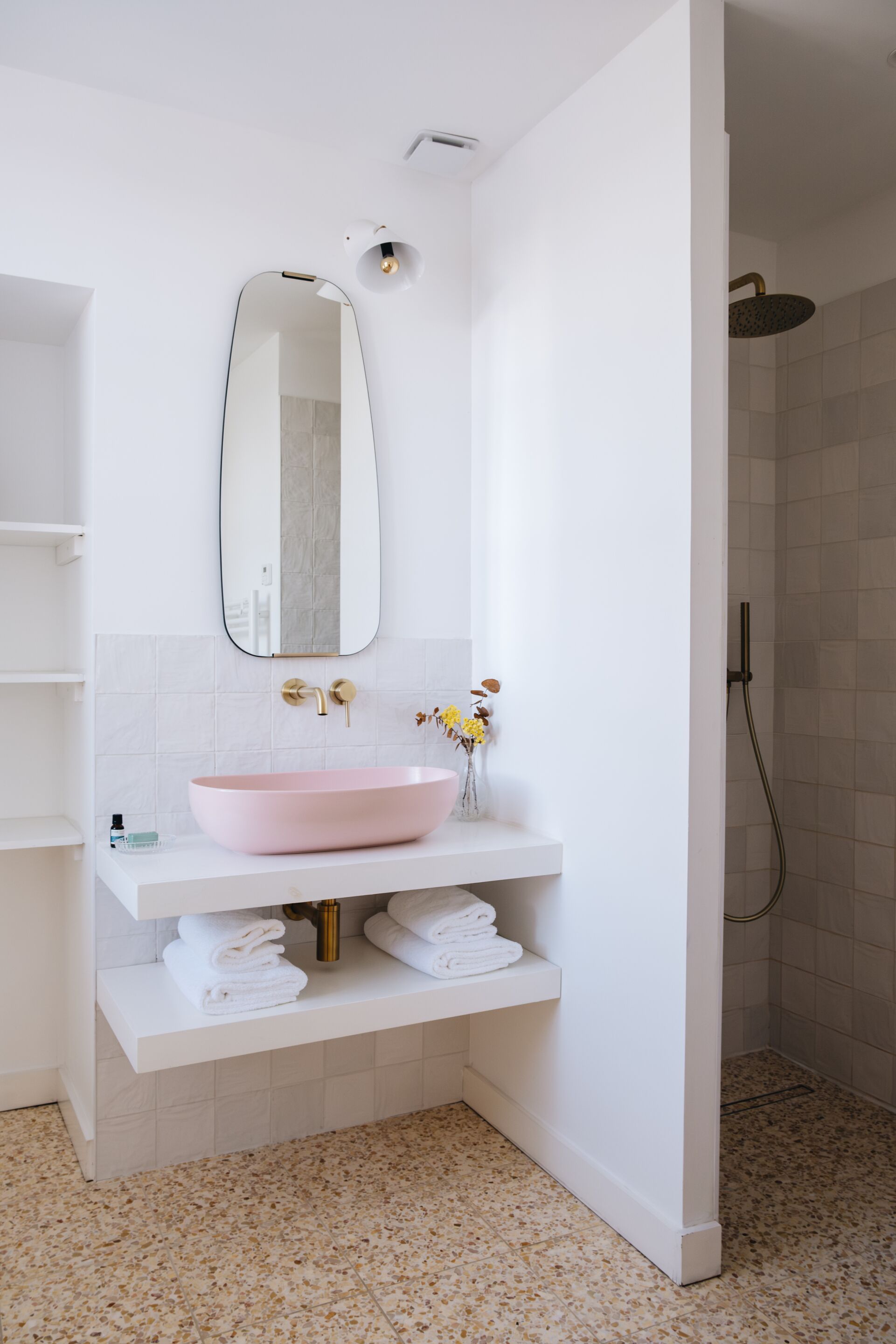 A bathroom with a white vanity, a pink sink, a mirror, and a shower area.