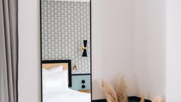 A mirror reflecting a bed, a nightstand, and a vase with pampas grass.