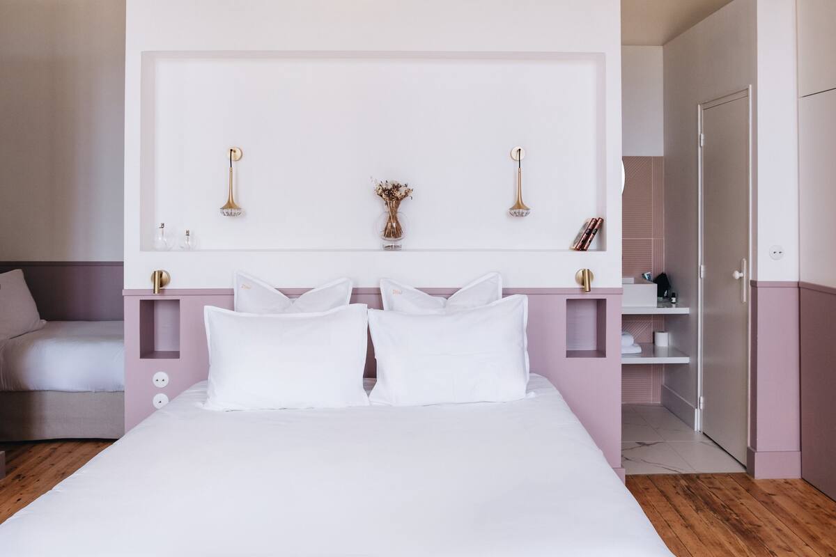 Un dormitorio con cama, mesitas de noche, cómoda, espejo y puerta.
