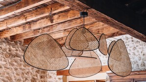 Un coin repas rustique avec une table et des chaises en bois, un luminaire suspendu au plafond fait de fibres tressées et un mur en pierre.