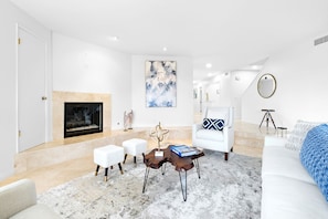 Een moderne woonkamer met een open haard, witte meubels en een groot abstract schilderij.