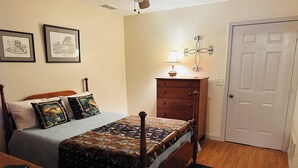 A bedroom with a wooden bed, a nightstand, a dresser, a lamp, and a door.