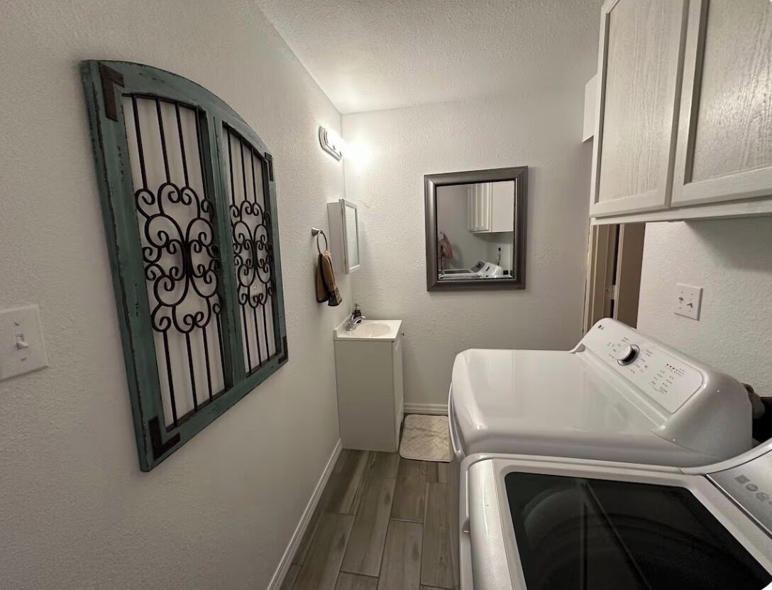 A compact laundry room with a washing machine, a sink, and a mirror.