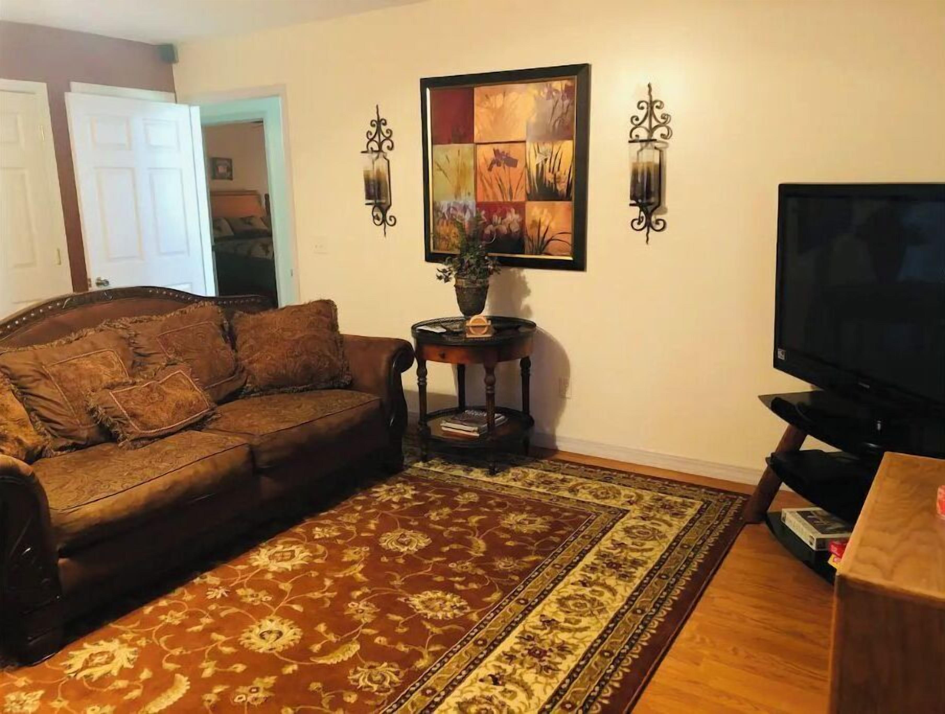 A living room with a brown sofa, a patterned rug, a television, and wall-mounted sconces.