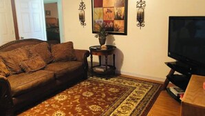 A living room with a brown sofa, a patterned rug, a television, and wall-mounted sconces.