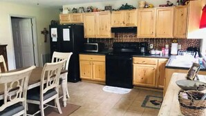 A kitchen with wooden cabinets, a black refrigerator, a microwave, and a stove. There is a dining table with chairs.