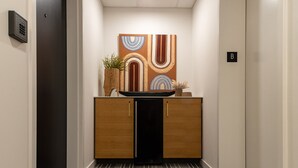 A hallway with a wooden cabinet, a potted plant, and a wall-mounted artwork. - The Finnley (Grand Rapids)