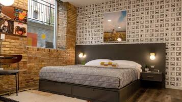 A bedroom with a brick wall, a bed with patterned bedding, a nightstand, and wall-mounted lights.