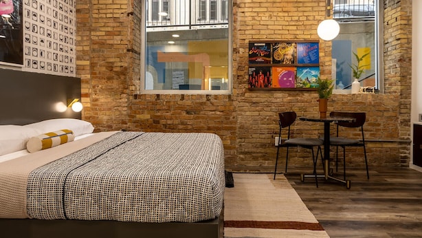 A bedroom with a brick wall, a bed, a desk, and a chair. - The Finnley (Grand Rapids)
