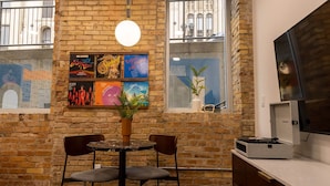 A brick-walled room with a round table and two chairs, a hanging light fixture, and a window with a plant. - The Finnley (Grand Rapids)