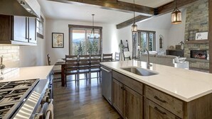 A modern kitchen with a large island, wooden cabinets, and a stone fireplace.
