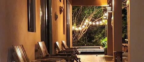 A covered outdoor seating area with wooden chairs and tables, a tiled floor, and string lights.