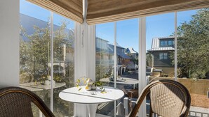 Une véranda dotée d’une table en verre et de chaises en osier, donnant sur un quartier résidentiel avec des maisons et des arbres.