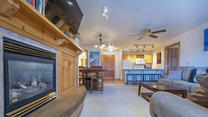 A living room with a fireplace, a sofa, a coffee table, and a kitchen in the background. - Recreation Headquarters! National Parks! Hot Tubs & Gym! On Teton Creek! Clean! (Driggs)