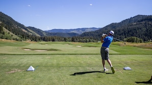 A golf course with a clear sky, a golfer in a blue shirt and cap, and a mountainous backdrop. - Recreation Headquarters! National Parks! Hot Tubs & Gym! On Teton Creek! Clean! (Driggs)