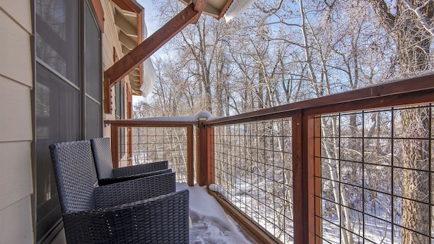 A balcony with wicker chairs, a wooden railing, and a view of a snowy forest. - Recreation Headquarters! National Parks! Hot Tubs & Gym! On Teton Creek! Clean! (Driggs)