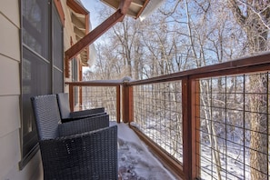 A balcony with wicker chairs, a wooden railing, and a view of a snowy forest.