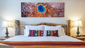 A bed with a colorful striped blanket, two bedside lamps, and a large painting above the bed. - Recreation Headquarters! National Parks! Hot Tubs & Gym! On Teton Creek! Clean! (Driggs)