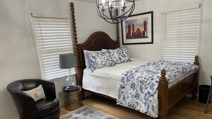 Une chambre à coucher avec un lit en bois, une chaise, une lampe, un tapis et un tableau représentant un paysage urbain.
