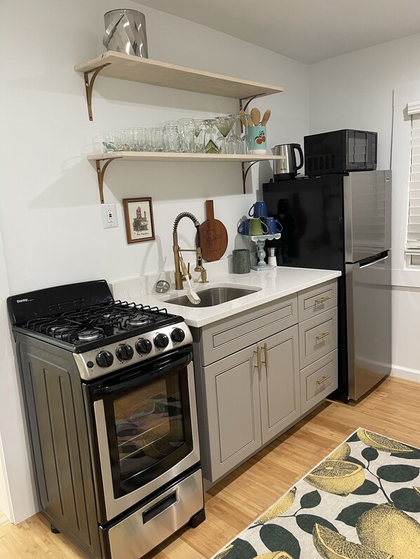 A compact kitchen with a gas stove, oven, stainless steel refrigerator, and a microwave.