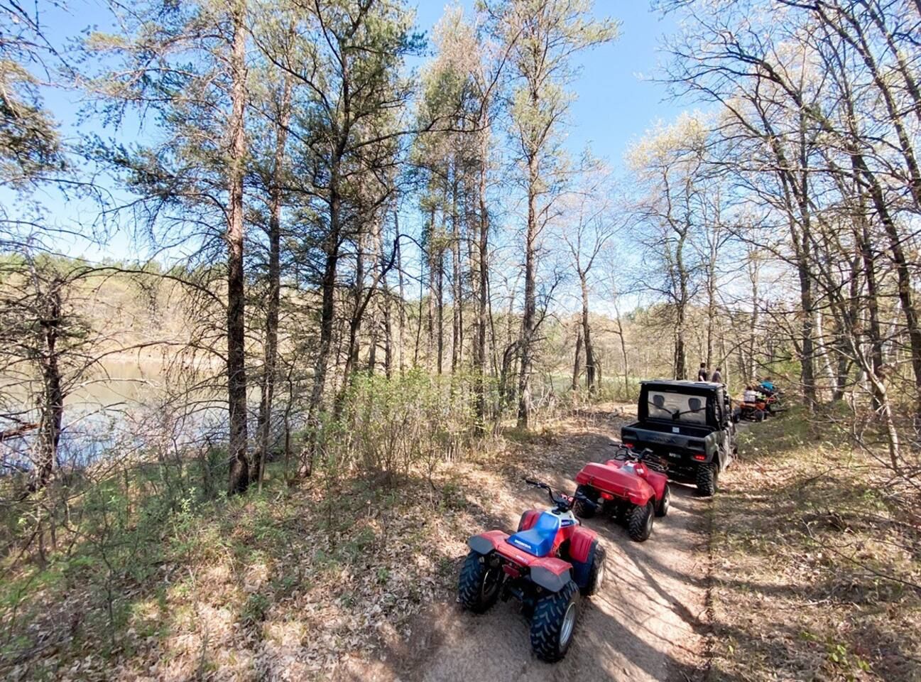 A forested area with a dirt path and ATVs.