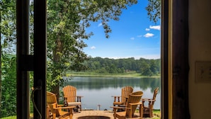 A lakeside view with wooden chairs and a fire pit, surrounded by trees and a clear sky. - Summer oasis w/NEW HOT TUB overlooking Fawn Lake with private beach, SUPs/Kayaks (Crosslake)