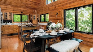 A wooden cabin-style kitchen with a dining area, large windows, and a view of greenery. - Summer oasis w/NEW HOT TUB overlooking Fawn Lake with private beach, SUPs/Kayaks (Crosslake)