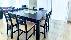 A dining area with a rectangular table and six chairs, a sofa, and a TV in the background.