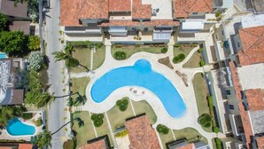An aerial view of a residential area with a swimming pool, palm trees, and houses with red-tiled roofs.